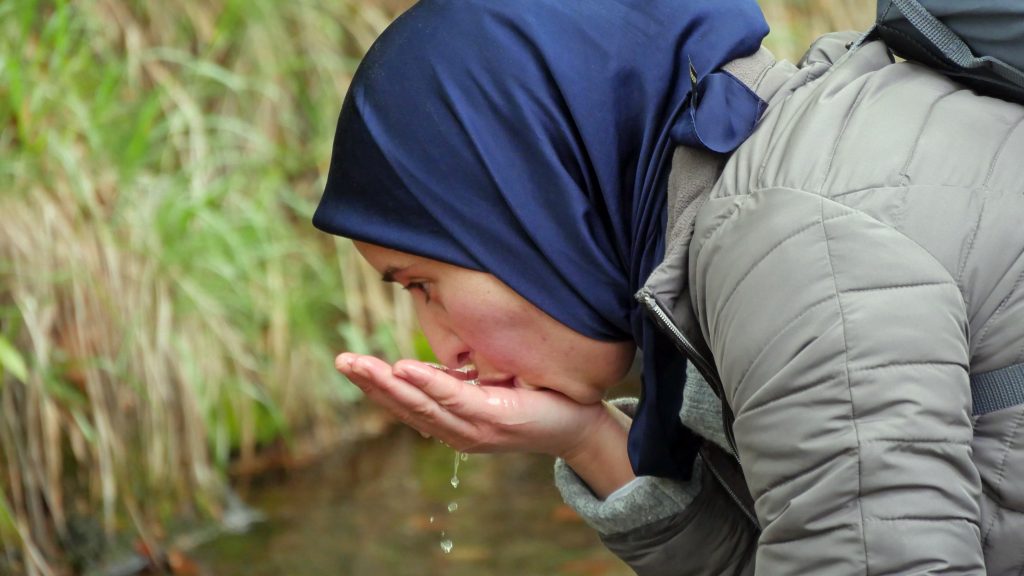 Eine Frau trinkt Wasser aus einem kleinen Bach.